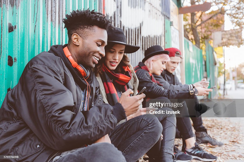 Gruppo multietnico di hipster all'aperto che usano i telefoni