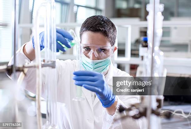 scientist pouring a chemical into a measuring cylinder - químico imagens e fotografias de stock