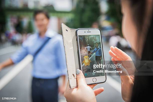 Woman plays Nintendo Co.'s Pokemon Go augmented-reality game, developed by Niantic Inc., on their smartphones on a street in the Akihabara district...
