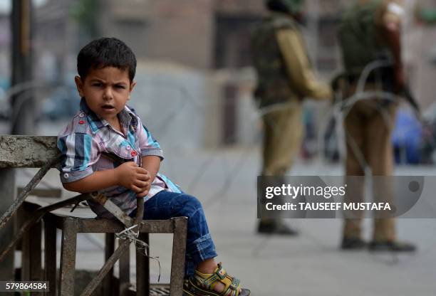 Kashmiri boy looks on outside a house as Indian paramilitary personnel stand guard during a seventeenth day of curfew in Srinagar on July 25, 2016....