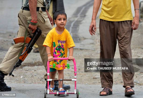 Kashmiri child plays in the street with his father as an Indian paramilitary trooper patrols past during a seventeenth day of curfew in Srinagar on...