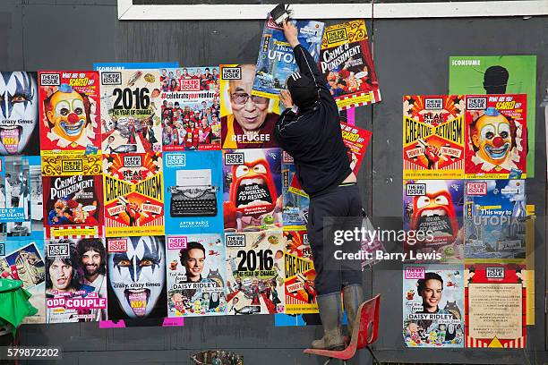 Big issue seller pasting up covers in the Shangri La field, Glastonbury Festival 2016. Glastonbury Festival is the largest greenfield festival in the...