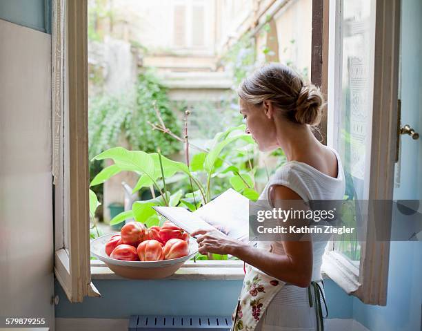 woman reading cookbook at open kitchen window - hair bun back stock pictures, royalty-free photos & images