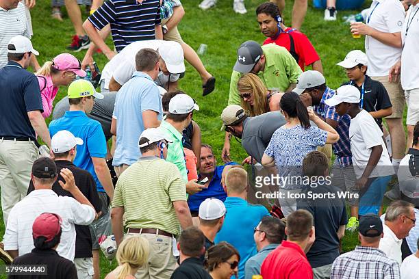 Fan, wearing a blue shirt, lies on the ground and is attended to by tournament medical personnel after being struck in the head by an errant fairway...