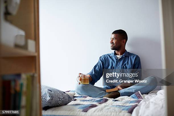 black man drinking tea and reading on bed - man having tea stock pictures, royalty-free photos & images