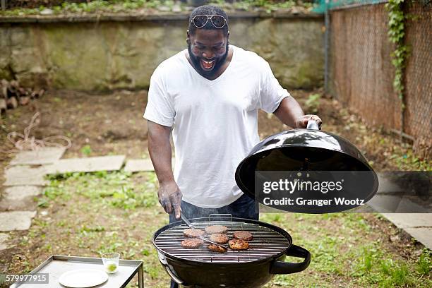 black man grilling hamburgers at backyard barbecue - one mid adult man only stock pictures, royalty-free photos & images