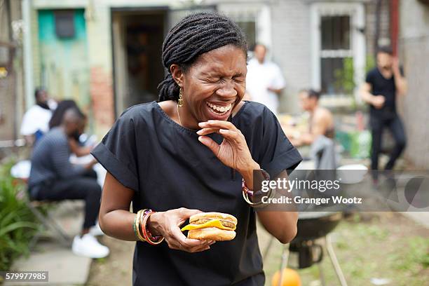 african american woman eating at backyard barbecue - burger on grill photos et images de collection