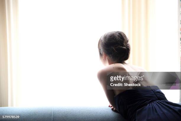 rear view of woman in evening gown looking out window - ballkleider stock-fotos und bilder