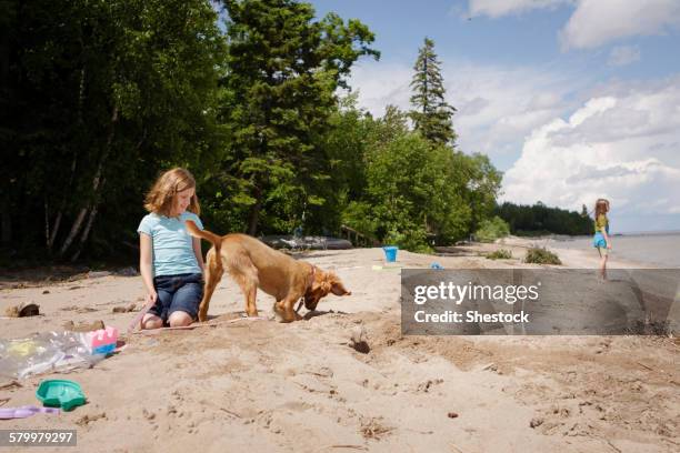 caucasian girl and puppy playing on beach - digging beach photos et images de collection