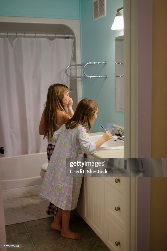 Caucasian sisters brushing teeth in bathroom