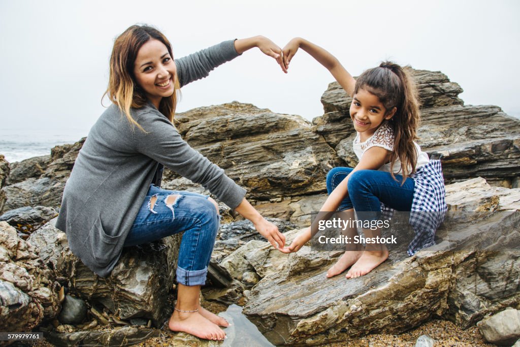 Hispanic mother and daughter making heart shape in tide pools