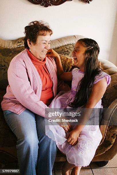 hispanic grandmother and granddaughter laughing on sofa - chubby granny stock pictures, royalty-free photos & images