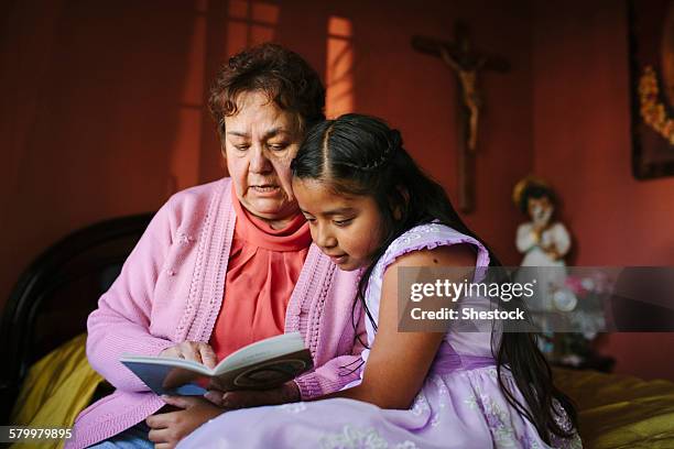 hispanic grandmother and granddaughter reading book on bed - multi generation family thinking stock pictures, royalty-free photos & images