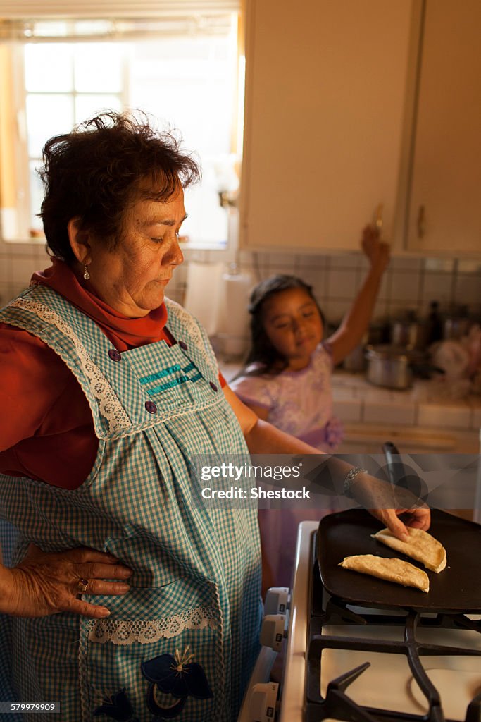 Hispanic woman cooking for granddaughter in kitchen