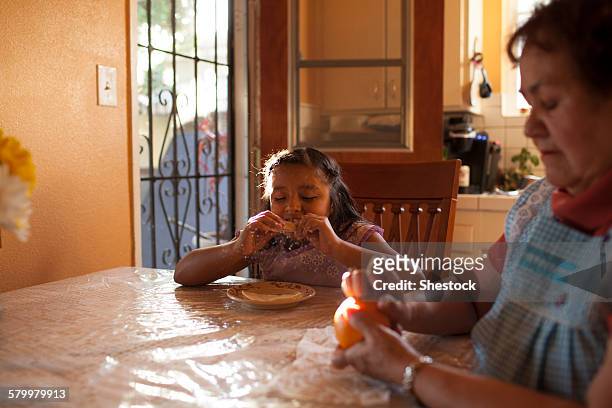hispanic grandmother and granddaughter eating in kitchen - chubby granny stock pictures, royalty-free photos & images