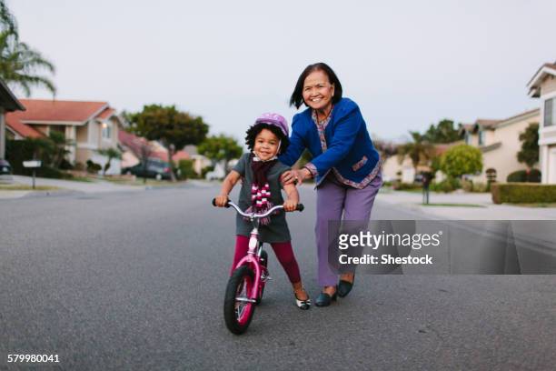 grandmother teaching granddaughter to ride bicycle on suburban street - fahrrad fahren großeltern mit kind stock-fotos und bilder