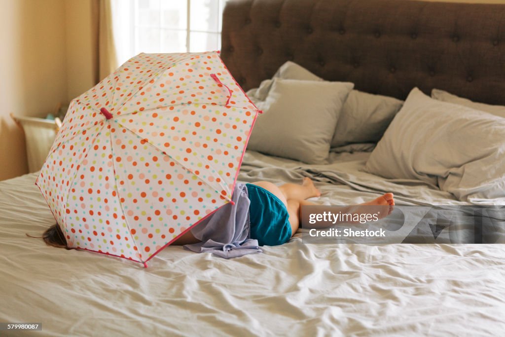 Caucasian girl playing with umbrella on bed