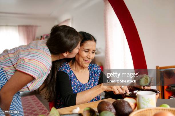 woman kissing grandmother cooking in kitchen - hispanic grandmother stock pictures, royalty-free photos & images