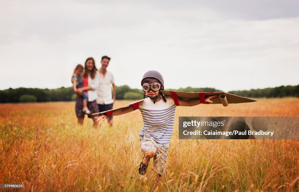 Playful boy with wings in aviators cap and flying goggles in field