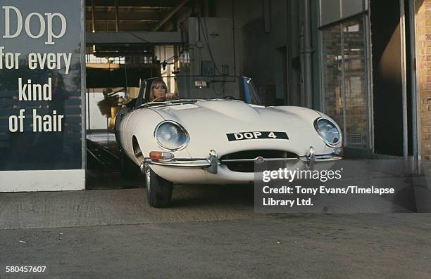 English model Pattie Boyd filming a commercial for Dop Pearlized Shampoo by L'Oreal, UK, 1966. Here she exits a car wash in a Jaguar E-type roadster...