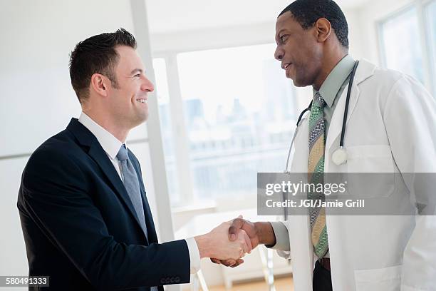 businessman and doctor shaking hands in office - medical thank you imagens e fotografias de stock