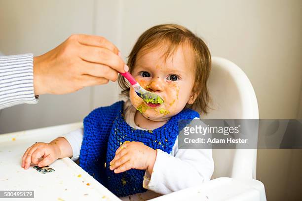 mother feeding baby girl in high chair - femme bras tendu cuillère photos et images de collection