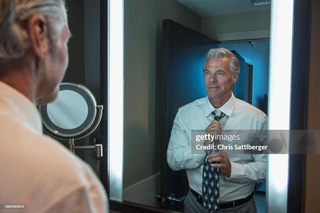 Caucasian businessman adjusting tie in mirror