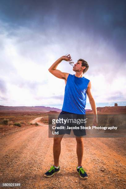 caucasian athlete drinking water bottle in desert landscape - mann wasser trinken sport stock-fotos und bilder