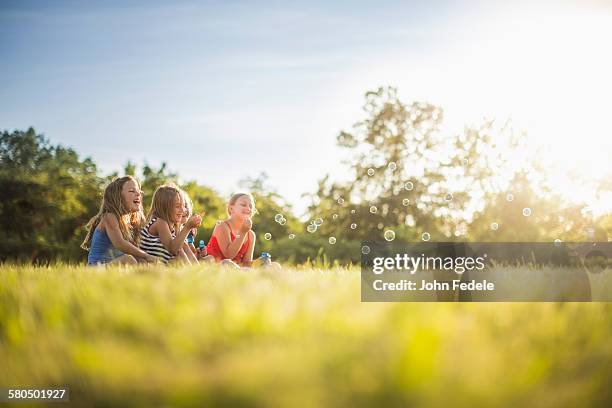 girls blowing bubbles in grass field - happy family grass stock-fotos und bilder