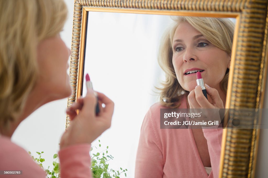 Caucasian woman applying lipstick in mirror