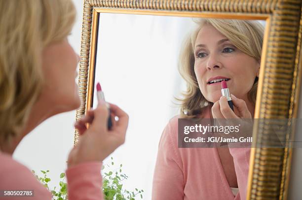 caucasian woman applying lipstick in mirror - only mature women stock pictures, royalty-free photos & images