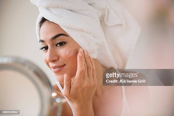 woman with hair in towel rubbing lotion on face - beautiful hair at home stock pictures, royalty-free photos & images
