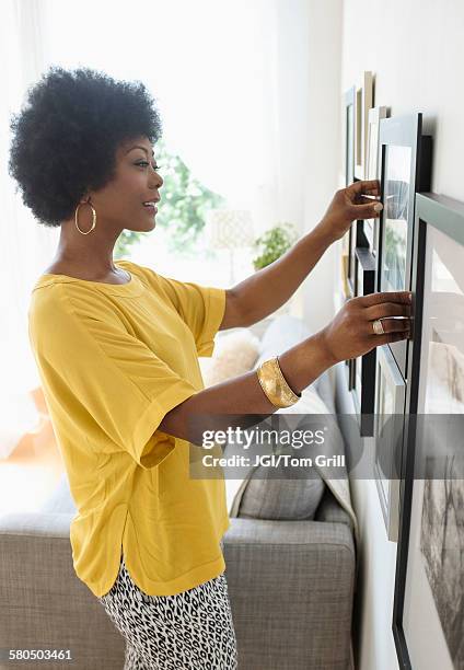 african american woman hanging pictures on living room wall - hanging picture frame stock pictures, royalty-free photos & images