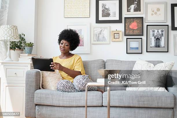 african american woman using digital tablet on sofa - endast en medelålders kvinna bildbanksfoton och bilder