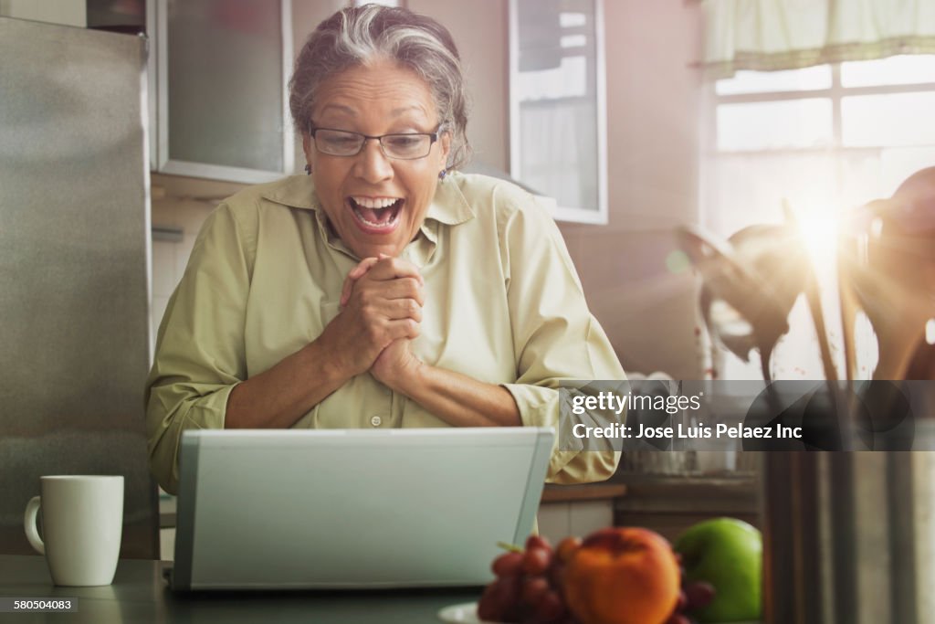 Surprised Hispanic woman with laptop in kitchen