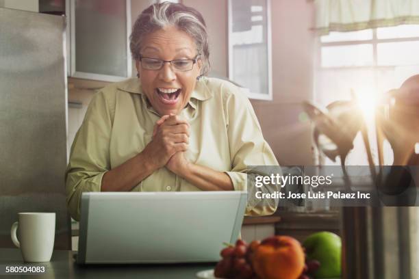 surprised hispanic woman with laptop in kitchen - excitement laptop stock pictures, royalty-free photos & images