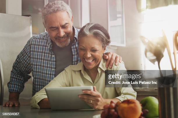 hispanic couple using digital tablet in kitchen - 60 65 man stock pictures, royalty-free photos & images
