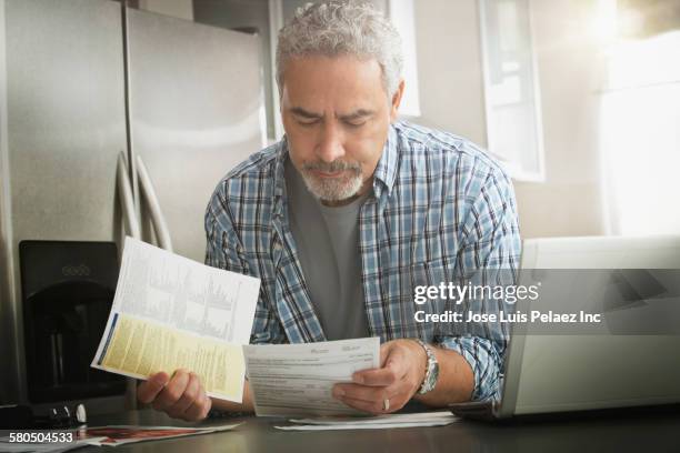 hispanic man paying bills on laptop in kitchen - kitchen front view stock pictures, royalty-free photos & images