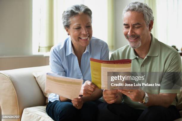 hispanic couple reading pamphlet on sofa - lebensversicherung stock-fotos und bilder