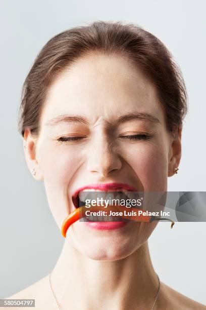 caucasian woman holding chili pepper between teeth - chili woman ストックフォトと画像
