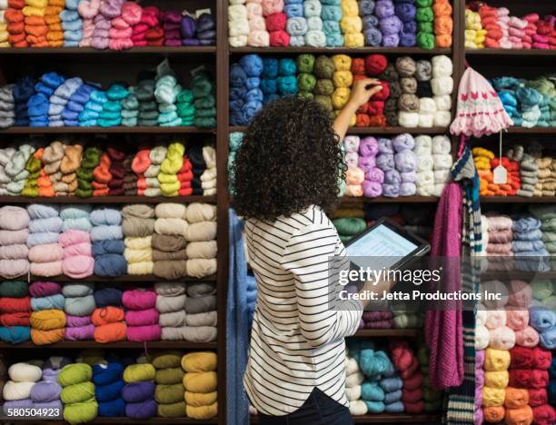 mixed race entrepreneur taking inventory in yarn store - lana fotografías e imágenes de stock