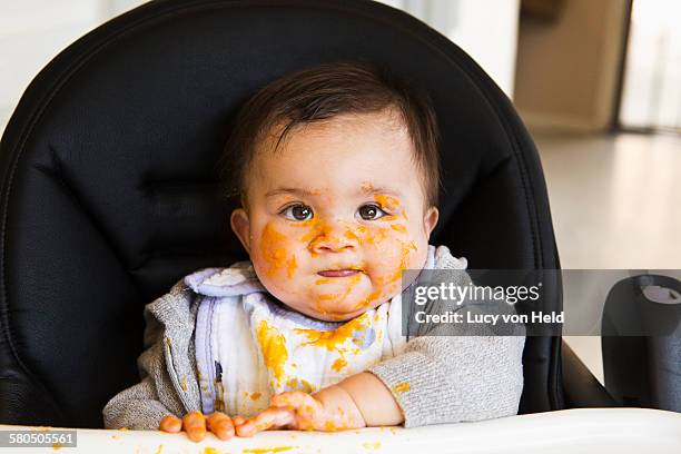 messy mixed race baby eating food in high chair - baby being held stockfoto's en -beelden