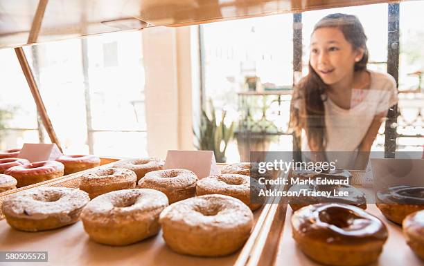 mixed race girl examining donuts in bakery - america patisserie stock pictures, royalty-free photos & images