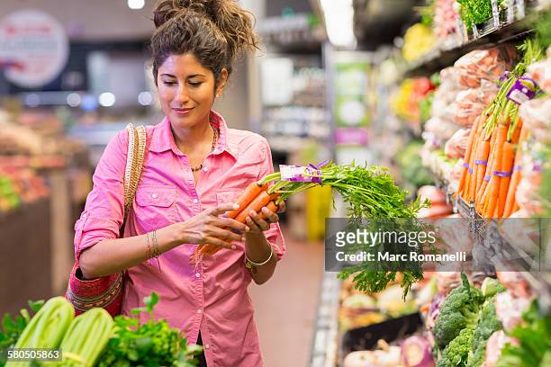 hispanic woman shopping at grocery store - diet carrot stock-fotos und bilder