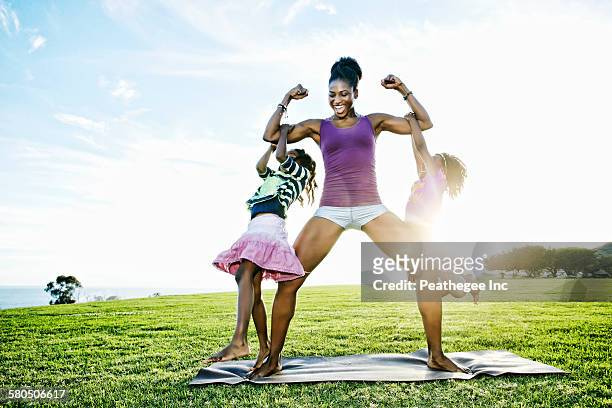 woman lifting children with biceps in park - family yoga photos et images de collection