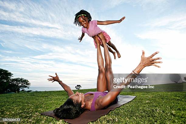 mother balancing daughter on legs in park - black shorts stockfoto's en -beelden