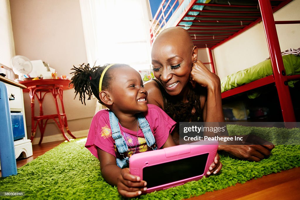 Black mother and daughter using digital tablet in bedroom