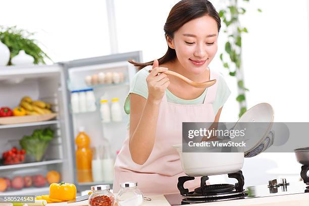 portrait of young woman cooking in kitchen - chinese soup photos et images de collection