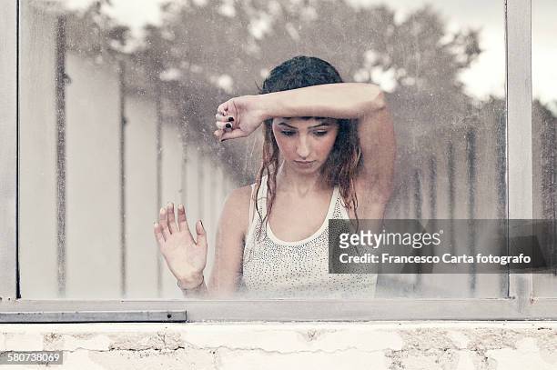 stressed young woman looking sadly through window - smart windows stockfoto's en -beelden