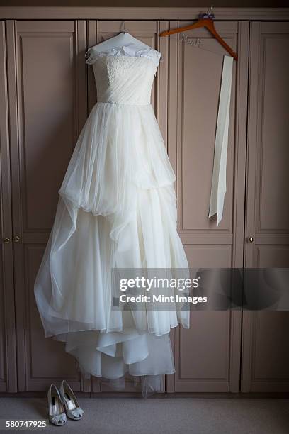 wedding dress hanging on a wardrobe door, wedding shoes on the floor. - wedding dress on hanger stock pictures, royalty-free photos & images